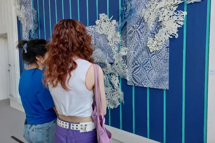 Two people are looking at an art work that fills an entire wall and is coloured in a bright blue.
